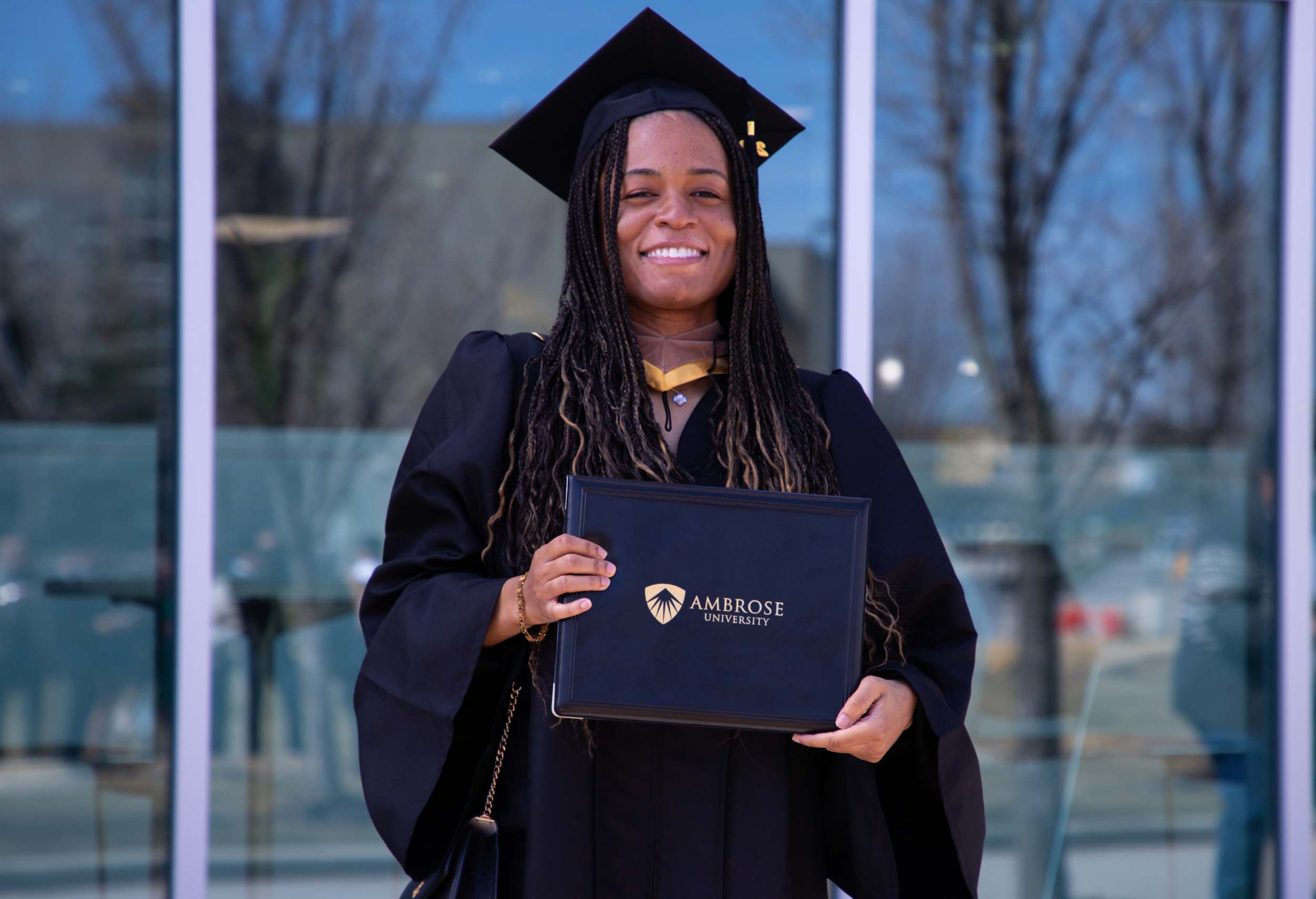 Woman standing in front of a window, holding an Ambrose University diploma